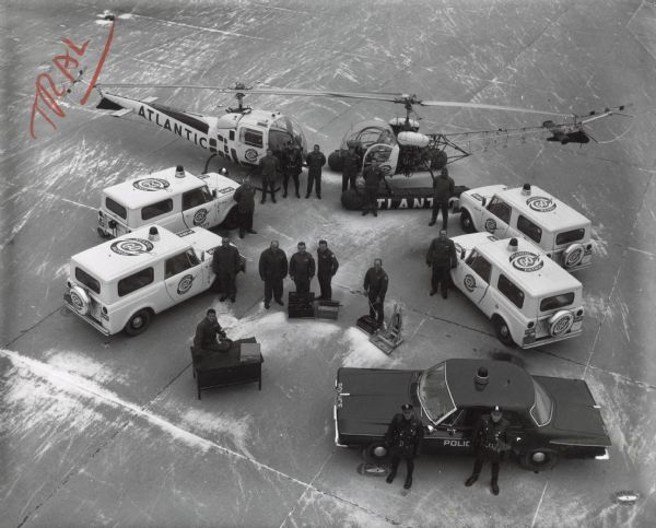 Elevated view of group of men posing with Atlantic GO Patrol vehicles. Includes four Scouts, two helicopters, and a police vehicle.