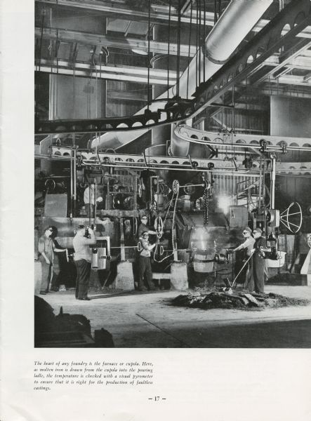 The furnace of a foundry at the Geelong Works, an International Harvester plant in Australia. Six men are posing around the foundry. Original caption reads: "The heart of any foundry is the furnace or cupola. Here, as molten iron is drawn from the cupola into the pouring ladle, the temperature is checked with a visual pyrometer to ensure that it is right for the production of faultless castings."
