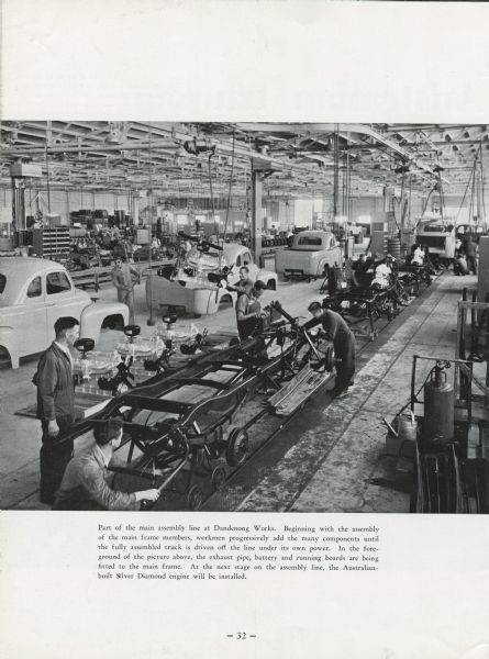 Truck assembly line at the Dandenog Works, an International Harvester plant in Australia. Seen are various stages of the assembly process of motor trucks. Original caption reads: "Part of the main assembly line at Dandenong Works. Beginning with the assembly of the main frame members, workmen progressively add the many components until the fully assembled truck is driven off the line under its own power. In the foreground of the picture above, the exhaust pipe, battery and running boards are being fitted to the main frame. At the next stage on the assembly line, the Australian built Silver Diamond engine will be installed."