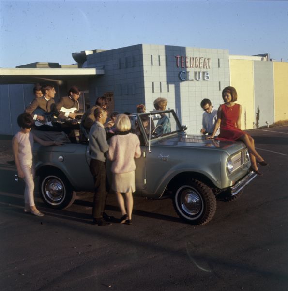 Group of people gathered in and around an International Scout pickup parked outside of the Teen Beat Club.