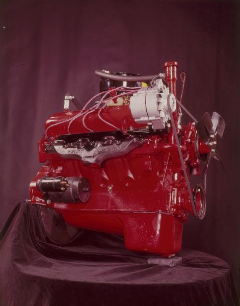 Engine painted red, displayed on a cloth covered table in front of a curtain. 