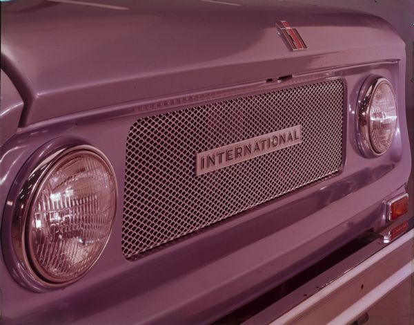 Close-up of front of Scout, including headlights, section of front hood with "IH" insignia, and "INTERNATIONAL" plate on grille.