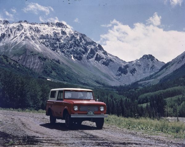 Scout being driven on gravel road with a mountain range visible in the background. 