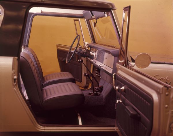 Passenger side view through open front door of front seats, steering wheel and dashboard of Scout Aristocrat. The driver's side door is also open.