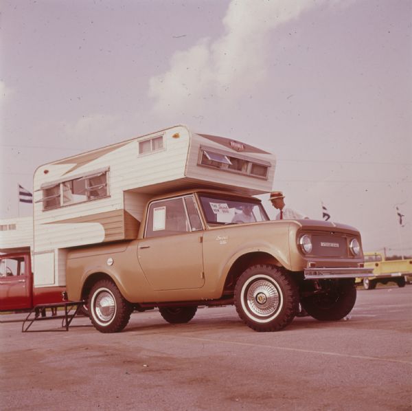 Scout 800 with Dreamer camper on truck bed and over cab. Other vehicles are parked in the background.