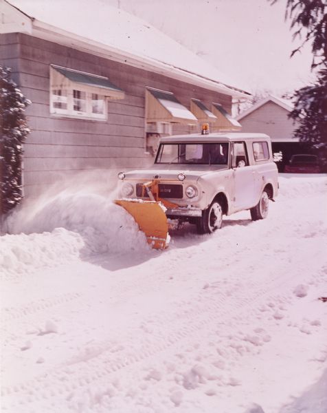 Man using a Scout 4x4 to plow a driveway near the side of a house.
