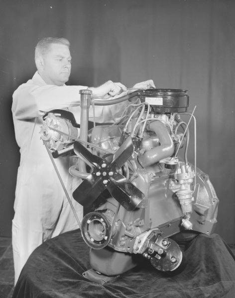 Man standing near Scout engine displayed on table draped with fabric.