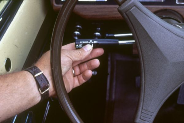 An unidentified man holds the cruise control lever mounted on the steering wheel column. It appears he is using his thumb to turn the control to "OFF."