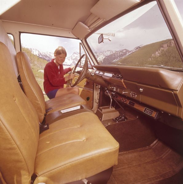 View from open passenger side door of a women getting into the driver's seat of a Scout. In the background are mountains.