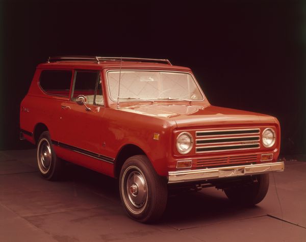 Three-quarter view from passenger side of red Scout II parked indoors. Red topper with roof rack.