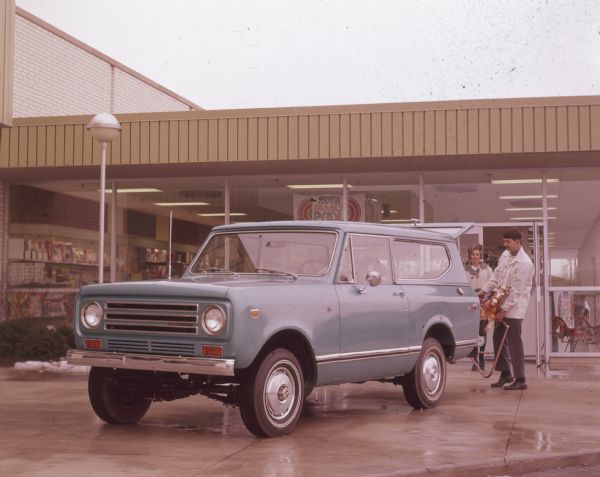 Man and woman loading toy rocking horse into a blue Scout II parked in front of a store.