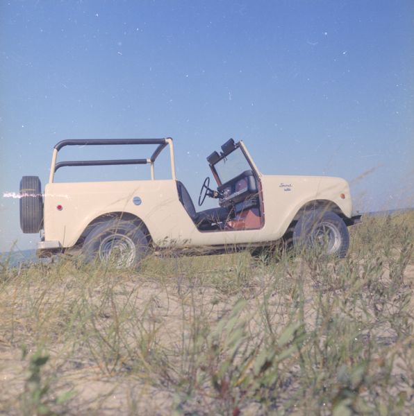 Passenger side view of Scout parked on beach. The Scout has a windshield and roll bars in place, but no doors. The ocean is in the background.
