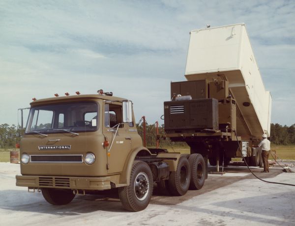 Three-quarter view from front of left side of COF-1810A Cargostar with Missile-Launch Cell in half-open position parked outdoors. A man is standing near a control panel on the right. Painted under driver's side door window is: "US ARMY."