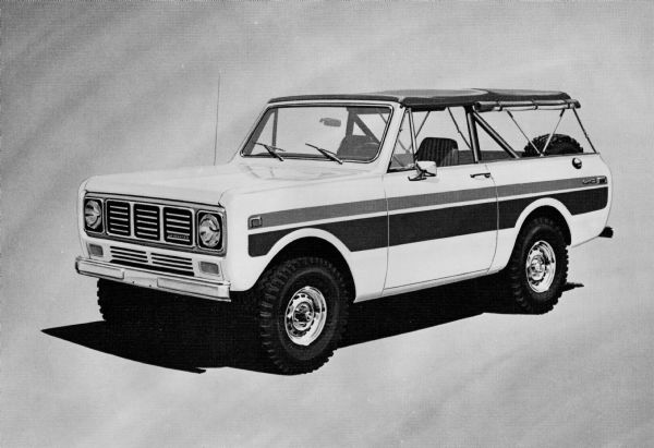 Three-quarter view from front of drivers side of the International Harvester Spirit Scout. Original caption reads: "(Photo #TF-1340)-- New 'special edition' International Scout models for 1976 include the 'Spirit' (shown), 'Patriot' and 'Sno-star.' All three models are painted white and feature distinctive red and blue striping treatments for a special Bicentennial theme. In addition, the Spirit has a blue 'soft' convertible top and is available as a 100-in wb. Scout II compact. The Sno-star is a 118-inch Scout Traveler station wagon and is patterned after the official U.S. Ski Team Vehicles. TD-3894 12/3/75."