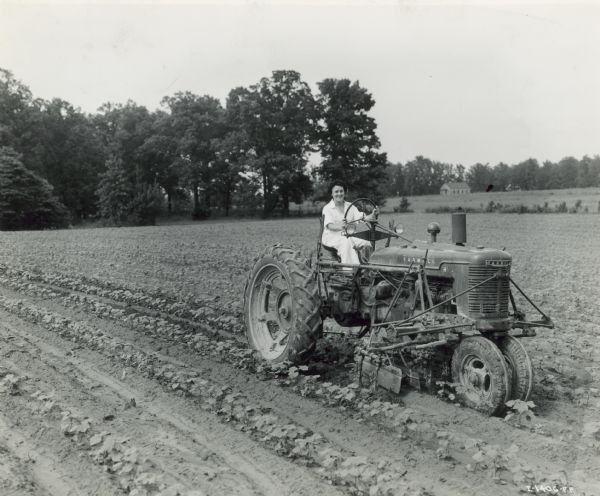Three-quarter view from front left of a woman on a Farmall H tractor in a field. Caption: "A very successful tractorette class of twenty women was organized by Hinton & Hutton, of Collierville, 23 miles east of Memphis, Tennessee. A prominent member of the class was Mrs. John T. Shea who is shown solo in cotton field on her 150-acre plantation in I-1405-FF, I-1406-FF, and I-1407-FF and who regularly operates the tractor."
