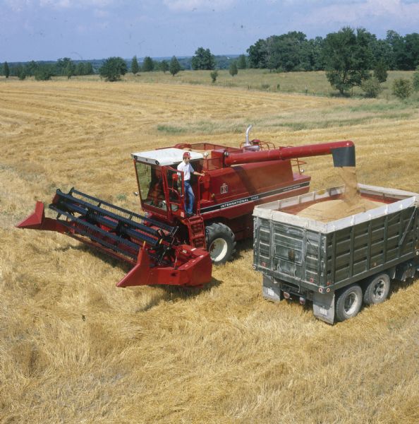 Elevated view of man using a International Harvester 1460 combine (harvester-thresher) in a field. An IH truck is parked beside the combine.