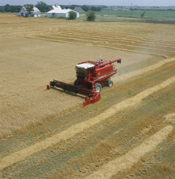 Elevated view of man using a 460 combine in a field. In the background are farm buildings.