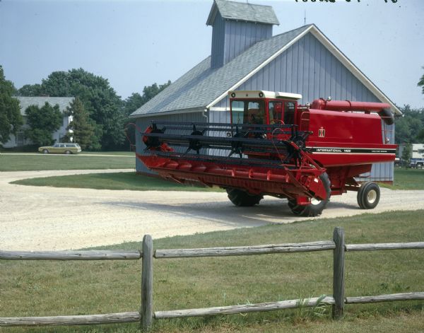 View over fence towards a 1420 axial-flow combine parked in a gravel driveway in front of a farm building.