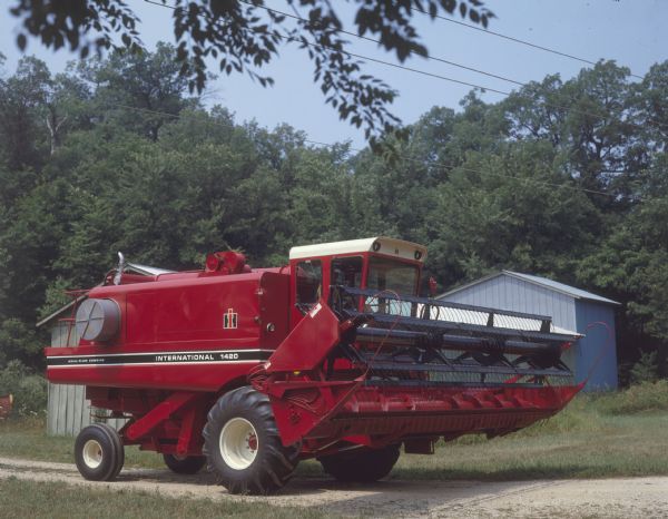 Three-quarter view from right front of a 1420 axial-flow combine parked in front of a farm building.