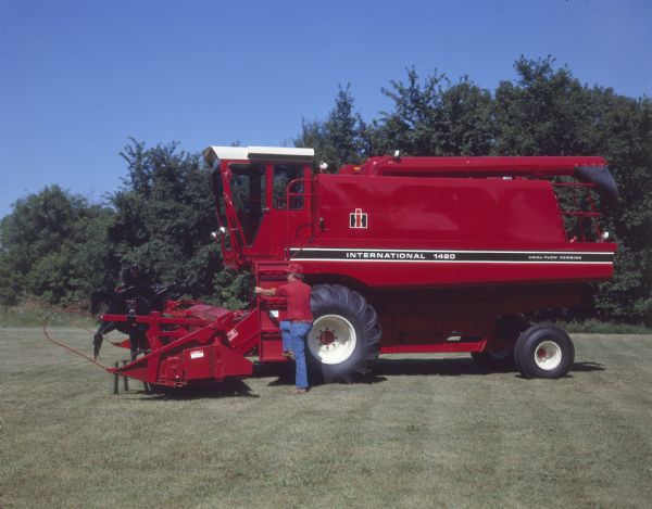 Left side view of a man posing standing at the bottom of the steps to the cab of a 1420 axial-flow combine.