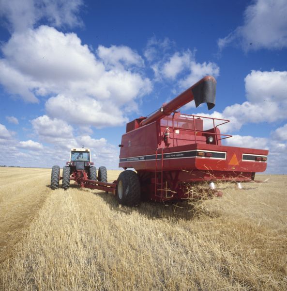 Rear view of a 1482 pull-type axial-flow combine pulled by a 1086 tractor in a field. White clouds and blue sky are visible in the background. 