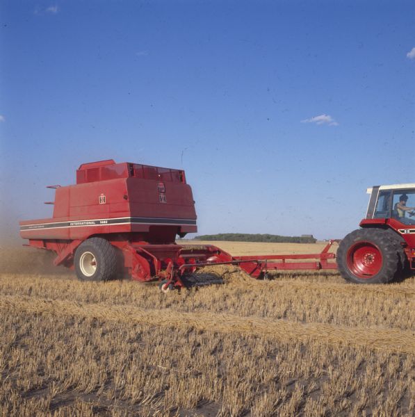 Right side view of a man using a tractor to operate a 1482 pull-type axial-flow combine in a wheat field.