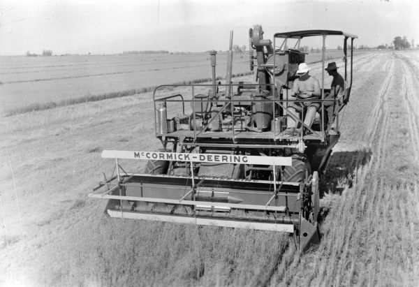 Front view of a McCormick-Deering self propelled combine.  Picture shows two men, a driver and bagger, atop the combine. 