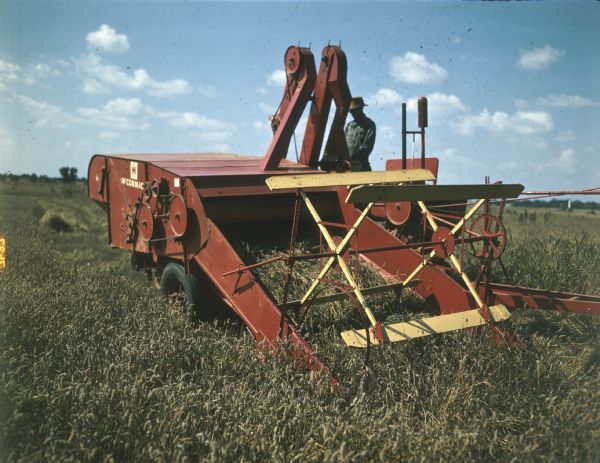 View of a man standing behind a McCormick combine in a field.