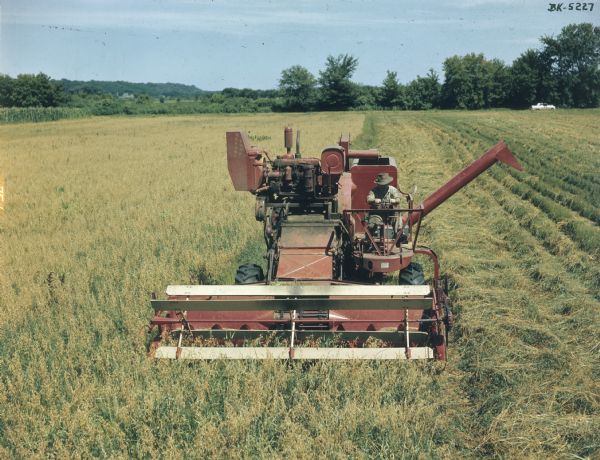 Slightly elevated view from front of a man on a McCormick combine in a field.