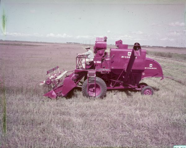 Left side view of a man using a McCormick combine in a field.
