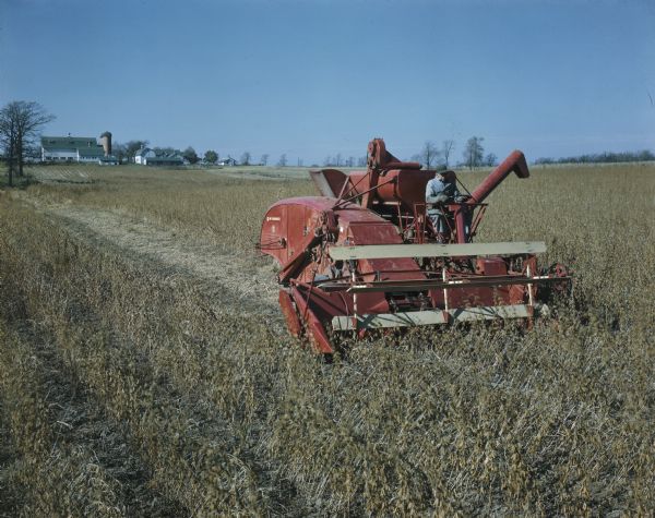 Three-quarter view from front right of man using a McCormick 125 SP combine in a field. Farm buildings are in the background.