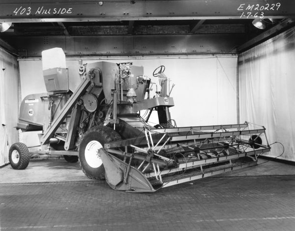 Three-quarter studio shot from the front right of an International 403 Hillside self-propelled combine. White seamless cloth and studio lights are visible. 
