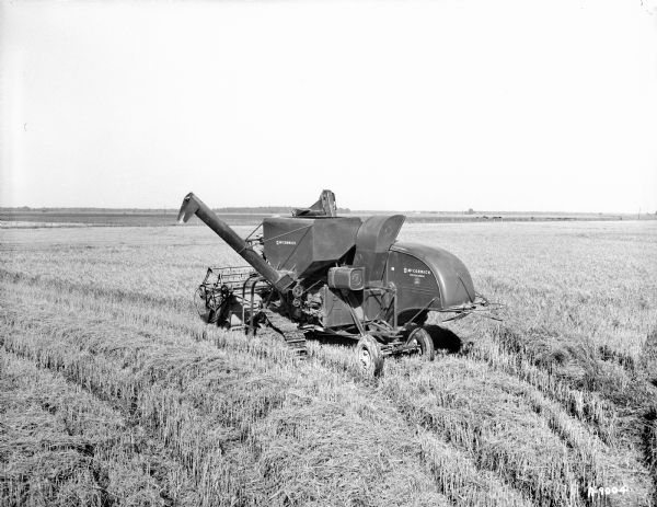Three-quarter view from left rear of man operating a McCormick rice special combine 125 SPV in a field.