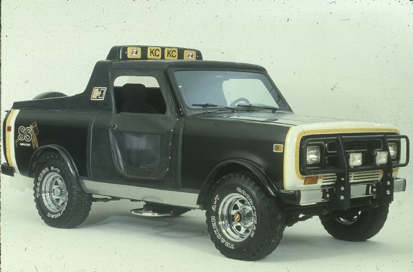 Three-quarter view from front of passenger side of Scout. Detachable door is in place, cab roof has added element, front grille with headlights attached. Rear of Scout has a decal for "Shawnee Scout." On the roof are decals for "Hurst" and "KC." Goodyear A-T Tracker tires.