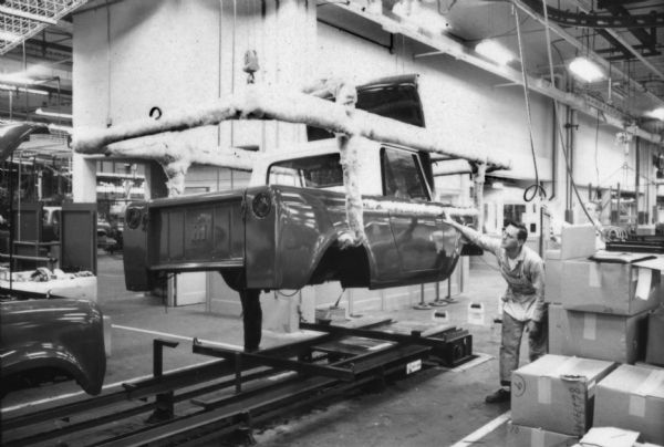 Man helping to move an International Scout body being lifted onto the next portion of its production stage. Assembly line image from International Harvester's Fort Wayne plant, subject of a 1961 article in <i>International Harvester Today</i> entitled: "The Scout."