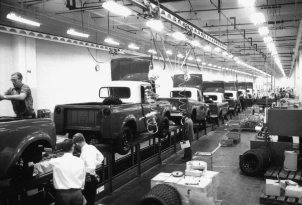 Slightly elevated view of International Scouts on assembly line. Men are working installing wheels as they near the end of the production process at the Fort Wayne plant. Assembly line image from International Harvester's Fort Wayne plant, subject of a 1961 article in <i>International Harvester Today</i> entitled: "The Scout."
