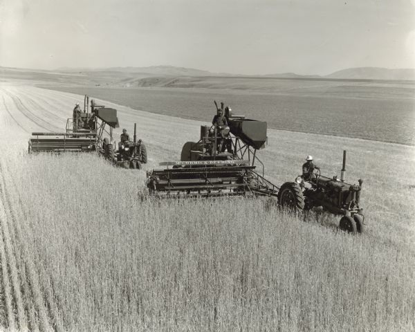 Elevated view of men using F-20 tractors to pull 12-foot experimental combines in a field.