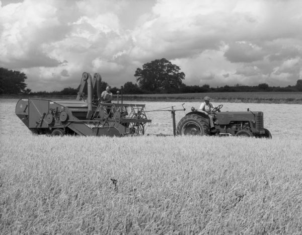 View across field towards a man driving a B-250 tractor pulling a man on a B-64 combine.