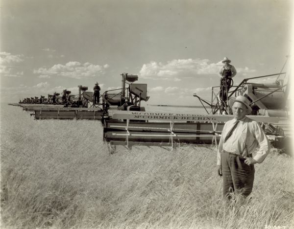 Mr. Louis Bertrand standing in front of his fleet of twelve McCormick-Deering 15-30 tractors and twelve McCormick-Deering No. 11 harvester-threshers. Men stand on each of the twelve harvester-threshers.