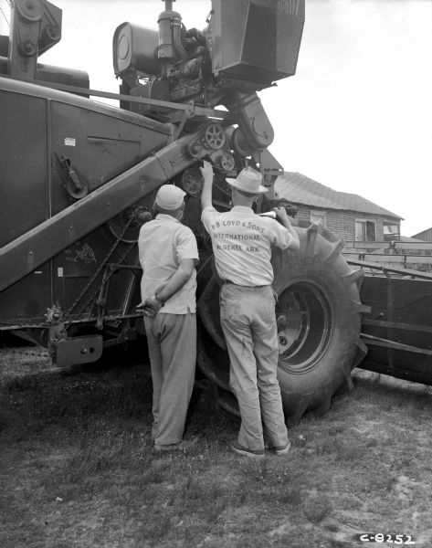 Two men are standing at the side of a combine looking at a mechanism.