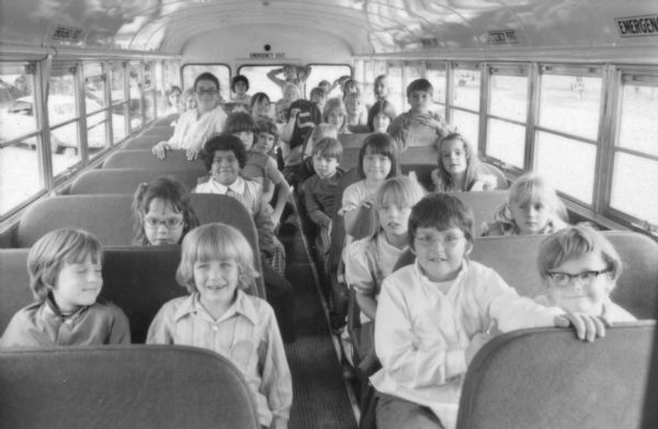 View from the front of a Kickert bus showing of a group of children and sitting in the bench seats, with one adult standing.