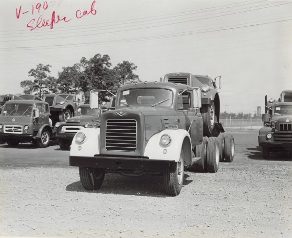 View of front of a V-190 with sleeper cab parked outdoors in a lot with other trucks at the Fort Wayne plant. The V-190 is pulling another V-190. RD Diesel to right. S Line and CO models to left.
