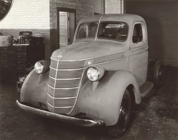 Styling study of front end for proposed 1937 D-Line 1/2 ton truck, clay mock-up. The final design for production changed from this with different headlight mounts, less stainless steel trim, and different name badges. This cab prototype had swing out windshield frame. Note scale model on a chest of drawers against the brick wall on the left.