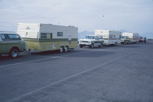View from side of road of a line of International vehicles pulling trailers. Mountains are in the background.