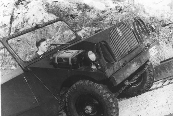 Three-quarter view form front passenger side of a man driving a 4x4 Scout chassis up an incline.
