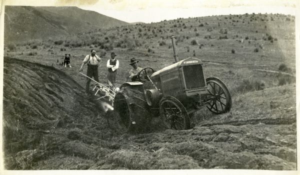 McCormick-Deering 10-20 tractor pulling a plow in New Zealand. Two men and a dog watch as the tractor ascends a hill.