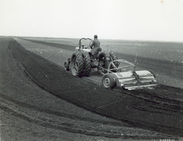 Three-quarter rear view from left side of a man driving a Farmall H pulling a Seaman tiller on the big Zellwood Farms.