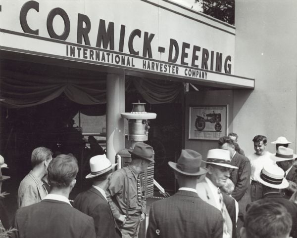 Slightly elevated view of men and boys standing at the entrance to a building with "Harvey Harvester." Sign above entrance to the building reads: "_Cormick-Deering, International Harvester Company."
