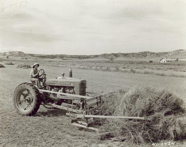 Man on a Farmall M with hay sweeper mounted on front.