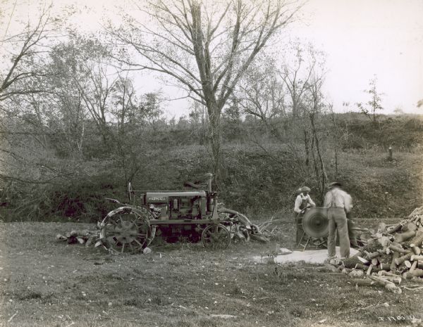 Two men in a field using a Farmall tractor to power a saw for cutting wood. Albert Sole.